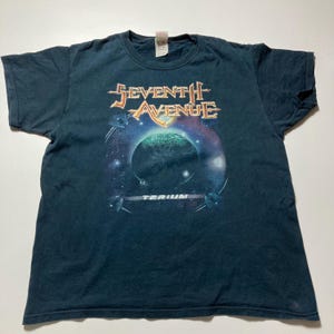 May include: Dark teal t-shirt with the band name "Seventh Avenue" in orange and gold lettering above a planet and space graphic. The word "Terium" is printed below the graphic.