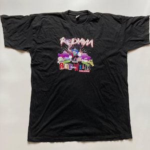 May include: Black t-shirt featuring a colorful graphic design. The design includes the text "REDMAN" in red and white, along with "RED WILD" and "THEE ALBUM". The graphic also features cartoon characters in various colors.