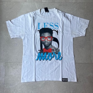 May include: White t-shirt featuring a graphic of a person wearing red glasses and a bow tie, with the words "LESS IS MORE" in blue. The shirt has a tag at the top and a brand label at the bottom.