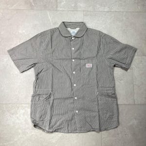 May include: A short-sleeved button-down shirt featuring a dark brown and white vertical pinstripe pattern, a rounded collar, and a chest pocket with a Smith's brand label. The shirt includes two large lower front pockets and white buttons.