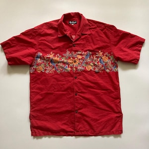 May include: Red short-sleeved shirt with a floral and bird design across the chest. The shirt has a button-down front and a collared neckline. The design features blue birds, orange and yellow flowers, and green leaves.