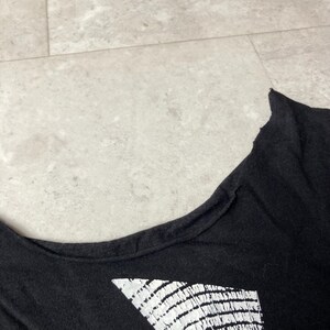May include: Black t-shirt with a white graphic design. The shirt has a scoop neck and a distressed, raw edge along the neckline. The graphic appears to be a geometric pattern.