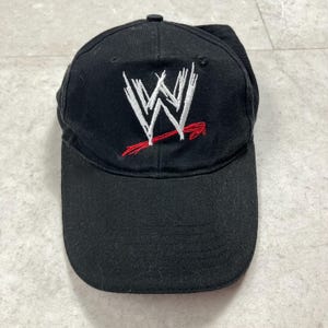 Puede incluir: Gorra de béisbol negra con el logotipo de la WWE bordado en blanco y rojo en la parte delantera. La gorra tiene una visera curva y un botón en la parte superior. El sombrero está hecho de tela duradera.