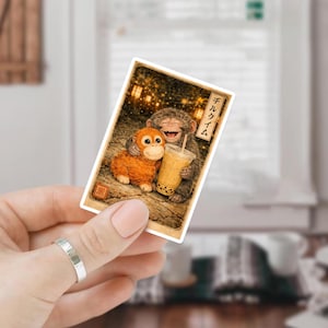 May include: A sticker featuring two cartoon monkeys, one hugging the other. The monkey on the right is holding a boba tea. The sticker has Japanese text and a warm color palette.