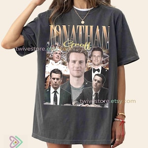 Puede incluir: Camiseta gris oscuro con un collage de imágenes de Jonathan Groff, con su nombre en letras doradas. La camiseta tiene una estética vintage, con la URL de la tienda Etsy impresa.