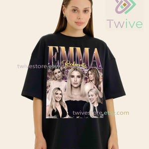 May include: Black t-shirt featuring a graphic of Emma Roberts with the name "EMMA" in gold lettering. The design includes multiple images of the actress. The shirt has a relaxed fit and short sleeves.