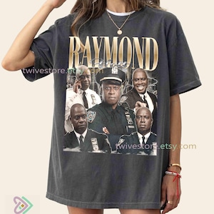 May include: Dark gray t-shirt featuring a graphic of several men in police uniforms and suits, with the name "RAYMOND" in gold lettering. The shirt has a vintage, slightly faded appearance.