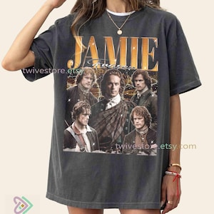 May include: Charcoal grey t-shirt with a gold-toned "JAMIE" graphic and a collage of actors. The shirt has a relaxed fit and is made of a soft material. The shirt is from twivestore.etsy.com.