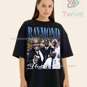 May include: Black t-shirt featuring a graphic of Raymond Holt from Brooklyn Nine-Nine. The design includes the name "Raymond" in blue, along with images of the character. The word "Hot" is also visible in the design.
