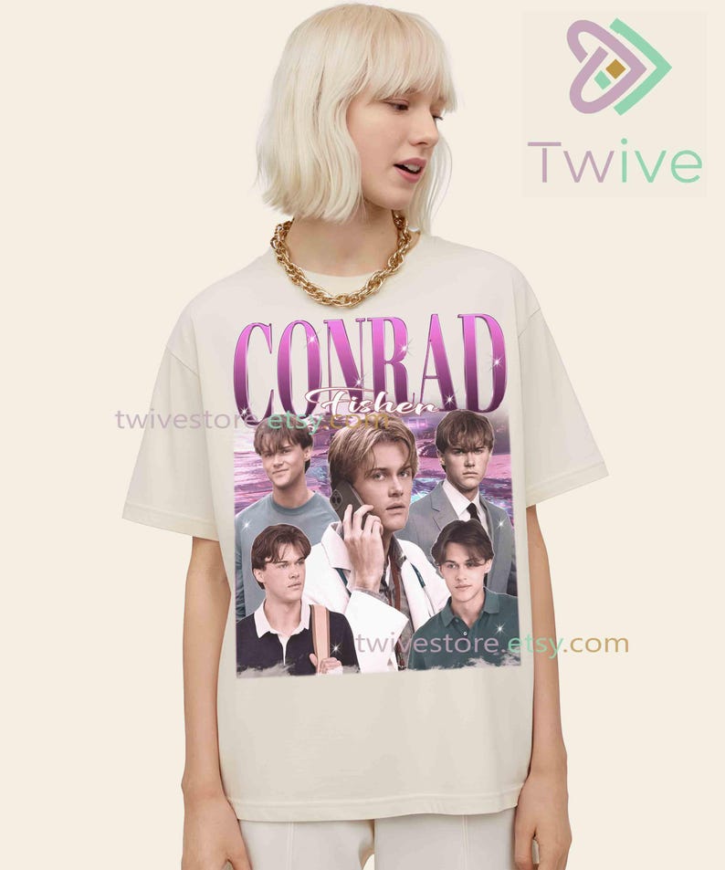 May include: Cream-colored t-shirt featuring a graphic of Conrad Fisher with a vintage aesthetic. The design includes the name "CONRAD Fisher" in a purple font, along with multiple images of the person. The shirt is worn by a person with blonde hair and a gold chain.