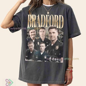 Puede incluir: Camiseta gris oscuro con la palabra "BRADFORD" en letras doradas sobre un collage de cinco hombres con uniformes de policía. La camiseta tiene un aspecto vintage y la URL de la tienda Etsy es visible.