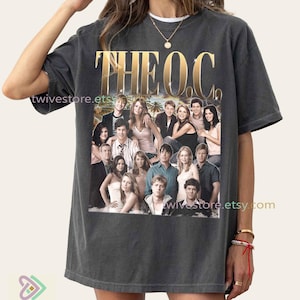 Puede incluir: Camiseta gris oscuro con una foto grupal del elenco de "The O.C." y texto dorado. La camiseta tiene un aspecto vintage, con "THE O.C." en dorado en la parte superior. La camiseta es de twivestore.etsy.com.