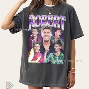 May include: Dark grey t-shirt with a collage of Robert Irwin images and the name "ROBERT IRWIN" in purple and white. The design has a vintage style and includes the Etsy shop name.