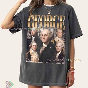 May include: Dark gray t-shirt featuring a portrait of George Washington and the text "GEORGE Washington" in gold lettering. The shirt has a vintage, distressed look, with the Etsy shop name "twivestore.etsy.com" printed on it.