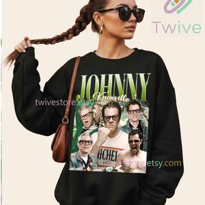 May include: Black sweatshirt featuring a collage of images of Johnny Knoxville with the text "JOHNNY Knoxville" in green and white. The sweatshirt is a crew neck style.