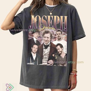 May include: Dark grey t-shirt with a graphic of Joseph Quinn, featuring the text "JOSEPH Quinn" in gold and purple. The design has a vintage aesthetic and includes images of Quinn and other actors.