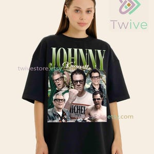 May include: Black t-shirt featuring a collage of images of Johnny Knoxville with the text "JOHNNY Knoxville" in green and white. The shirt is a crew neck and has short sleeves. The shirt is worn by a person.