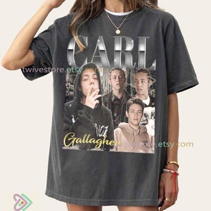 May include: Dark grey t-shirt with the name "CARL" in a chrome-effect font above a collage of images. Below the images is the name "Gallagher" in a gold script font. The shirt has a vintage, worn appearance.