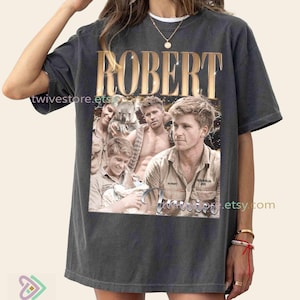 May include: Dark gray t-shirt featuring a collage of images and the name "ROBERT" in gold lettering. The images include a man with a koala and other outdoor scenes. The word "Irwin" is also visible.