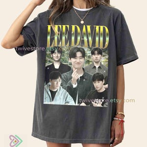 May include: Dark gray t-shirt featuring the text "LEE DAVID" in gold lettering above a photo of five men. The shirt has a vintage look and the Etsy shop name "twivestore.etsy.com" is printed on the shirt.