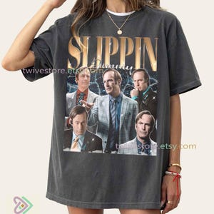 Peut inclure: T-shirt gris foncé avec l'inscription dorée "Slippin' Jimmy" et un collage d'images. Le design présente plusieurs images d'un homme dans différentes poses, sur fond d'éclairs.
