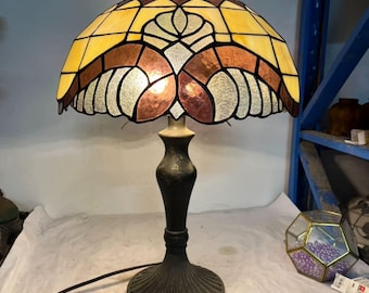 クラシックなステンドグラスの花のつぼみのテーブルランプ | しわのある白い布とアメジストの横で、静かなひとときを過ごす温かみのある琥珀色の光