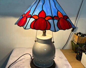 スカイブルーのランプシェードに映えるオレンジレッドの花の影 | トランペット型のステンドグラスと乳白色の陶器の台座が織りなすレトロな対比