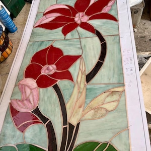 May include: Stained glass panel featuring a floral design with red, pink, and green hues. The flowers have detailed petals and are set against a light green background. The panel is framed with a copper border.