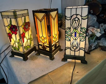 3 つのヴィンテージ ティファニー テーブル ランプが並んで立っています | 花柄、幾何学模様、純白の模様が織りなす温かみのあるシンフォニー。