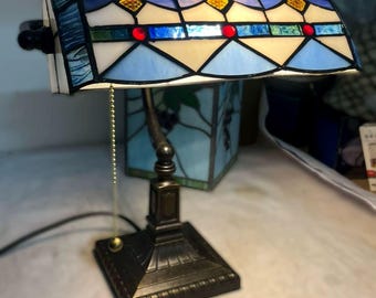 クラシックな青と白のティファニー テーブル ランプのクローズアップ | スカラップ ランプ シェードと金属チェーンのある静かなコーナー。