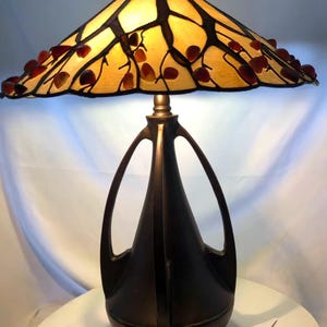 May include: A decorative table lamp with a stained glass shade featuring a leaf design. The shade is yellow with brown outlines and red leaf accents. The lamp has a dark bronze base with a unique, curved design.