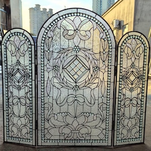 May include: A three-panel stained glass screen with an arched top. The design features intricate floral and geometric patterns in clear and frosted glass, outlined with black lines. The edges are trimmed with small, clear glass beads.