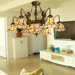 Peut inclure: Un lustre de style vintage avec une finition bronze et des abat-jours en vitrail. Le lustre comporte plusieurs lumières avec des motifs de feuilles blanches et vertes. Des figurines décoratives ornent le luminaire, ajoutant une touche d'élégance.