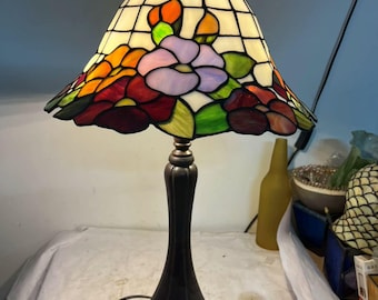 クラシックなステンドグラスの花柄テーブルランプ | 青い壁と明るい色のテーブルクロスを背景に、ピンクと紫の花が優しく咲いています。