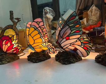 レトロな蝶型ガラスランプの実写画像｜暖かい光の下で、華やかな羽と暗いベースの静物画