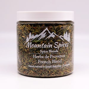 May include: A clear glass jar filled with dried herbs labeled "Mountain Spices Herbs de Provence French Blend Handcrafted in Small Batches - 2 ounces".