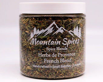 May include: A clear glass jar filled with dried herbs labeled "Mountain Spices Herbs de Provence French Blend Handcrafted in Small Batches - 2 ounces".