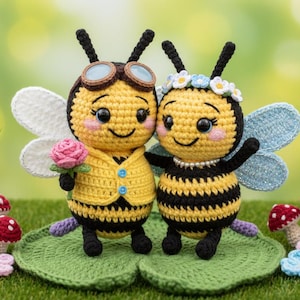 May include: Two crocheted bee dolls, one with goggles and a yellow waistcoat, holding a pink rose. The other bee wears a flower crown and a pearl necklace. They stand on green lily pads with crocheted mushrooms and flowers.