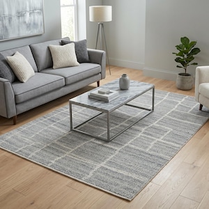Peut inclure: Salon moderne avec un canapé gris, des coussins et un tapis à motifs. Le tapis présente un motif géométrique gris et blanc. Une table basse en marbre et un parquet complètent la scène.