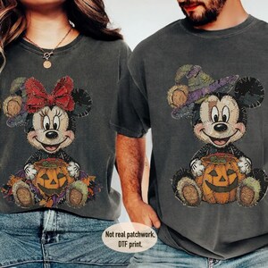 May include: Two charcoal gray t-shirts featuring a DTF print of cartoon characters sitting with pumpkins. The left shirt shows a character with a red bow, and the right shirt shows a character with a purple witch hat. Text reads: Not real patchwork. DTF print.