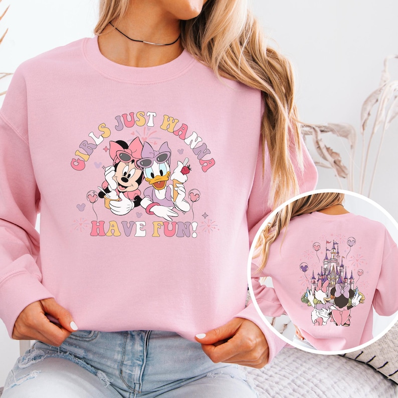 May include: A light pink sweatshirt featuring Minnie Mouse and Daisy Duck with sunglasses, holding treats, and the text "Girls Just Wanna Have Fun!". The back of the sweatshirt shows a castle and the same characters.