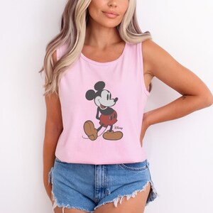 May include: Pink tank top featuring a graphic of Mickey Mouse in his classic pose. The cartoon character is depicted in black, red, and brown colors. The tank top is sleeveless and made of a soft material.