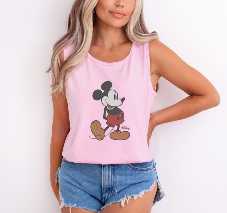 May include: Pink tank top featuring a graphic of Mickey Mouse in his classic pose. The cartoon character is depicted in black, red, and brown colors. The tank top is sleeveless and made of a soft material.