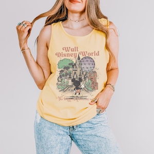 Puede incluir: Camiseta sin mangas amarilla con un dise&ntilde;o gr&aacute;fico retro de Walt Disney World, con Mickey Mouse y el texto "Walt Disney World" y "The happiest place on earth". El dise&ntilde;o es de estilo vintage. La camiseta est&aacute; hecha de un material suave.
