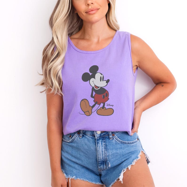 May include: A lavender tank top featuring a graphic of Mickey Mouse in his classic pose. The cartoon character is depicted in black, red, and tan colors. The tank top is sleeveless and made of a soft material.