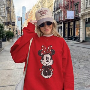 May include: A red Minnie Mouse sweatshirt with a distressed graphic. The image also shows a beige cap with the text "Western House Casino Las Vegas Nevada" and sunglasses.