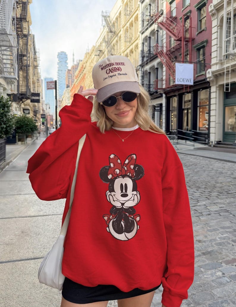 May include: A red Minnie Mouse sweatshirt with a distressed graphic. The image also shows a beige cap with the text "Western House Casino Las Vegas Nevada" and sunglasses.