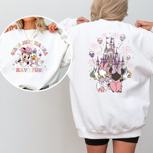 May include: White sweatshirt with a front graphic of Minnie Mouse and Daisy Duck, and the text "Girls Just Wanna Have Fun". The back features a castle design with the characters. The design includes pink, purple, and yellow accents.