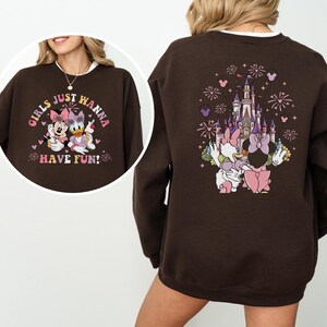 May include: A brown sweatshirt with a graphic of Minnie Mouse and Daisy Duck, and the text "GIRLS JUST WANNA HAVE FUN!" on the front. The back features a castle design with fireworks and the two characters.