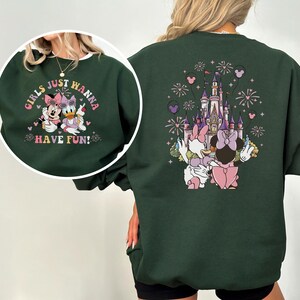 May include: Dark green sweatshirt with a cartoon design. The front features Minnie Mouse and Daisy Duck with the text "GIRLS JUST WANNA HAVE FUN!". The back shows a castle, fireworks, and more cartoon characters.